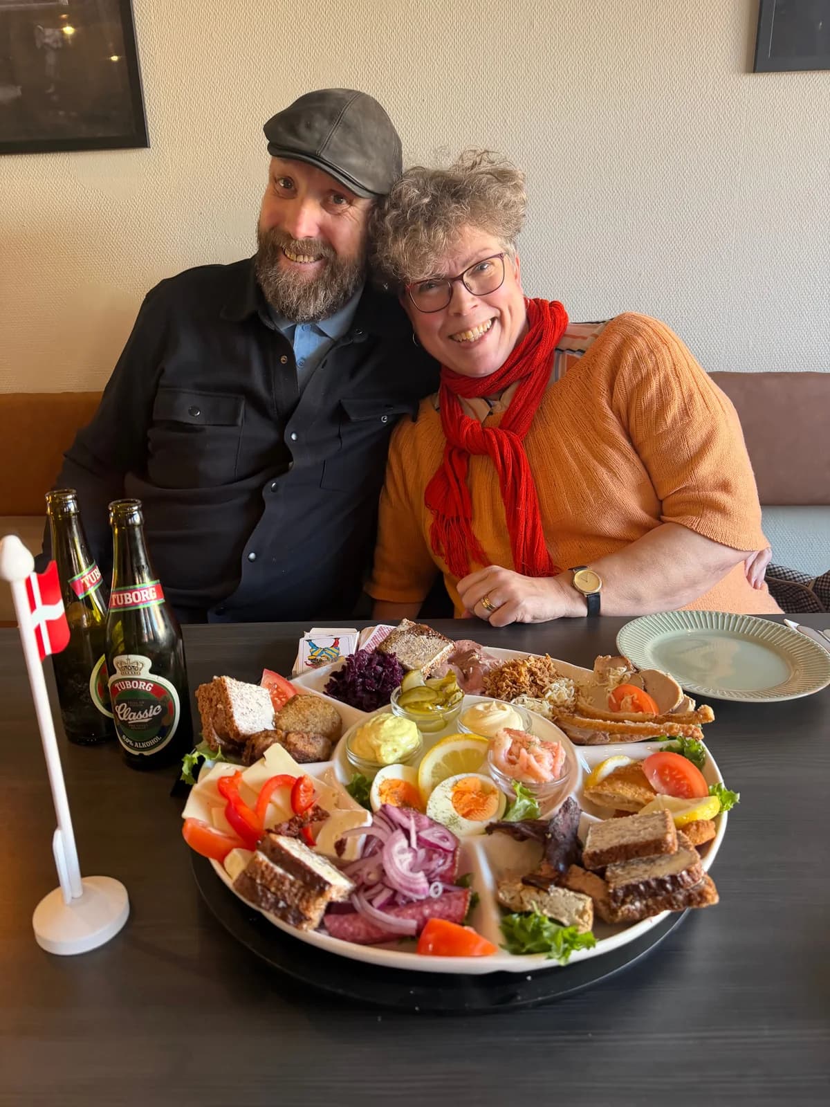 Två gäster vid bordet bakom en hyggetallrik för två med räkor, frikadeller, flæskesteg, rostbiff och leverpastej