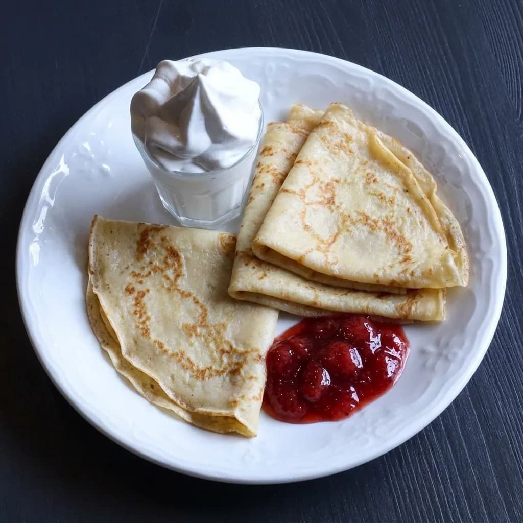 Pannkakor med sylt och grädde på en vit tallrik