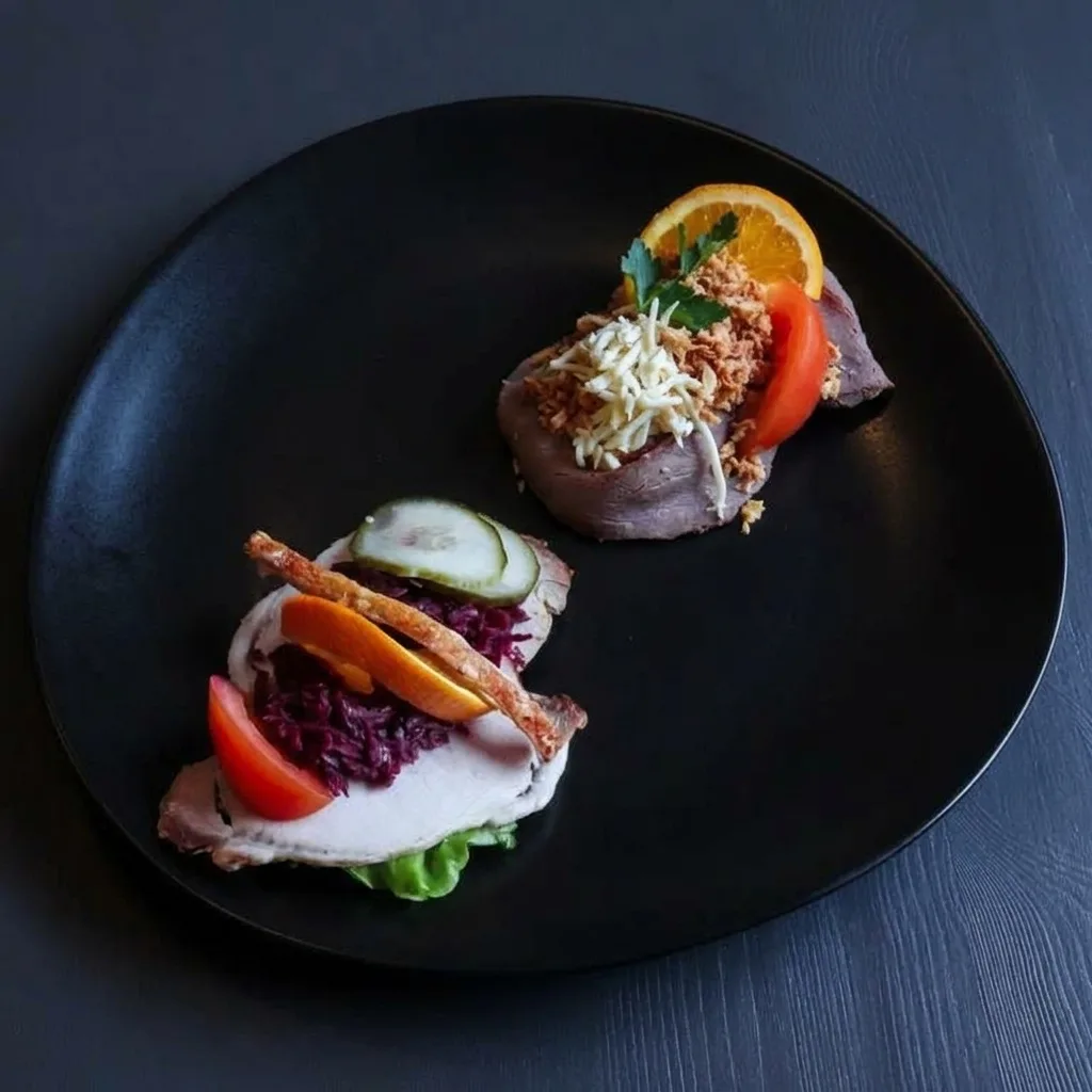 Två klassiska smørrebrød på en svart tallrik: flæskesteg med rödkål och rostbiff med remouladsås