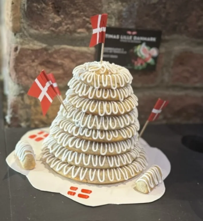 Hel kransekage staplad som ett torn med kristyr, danska flaggor i toppen och två ringar brutna bredvid